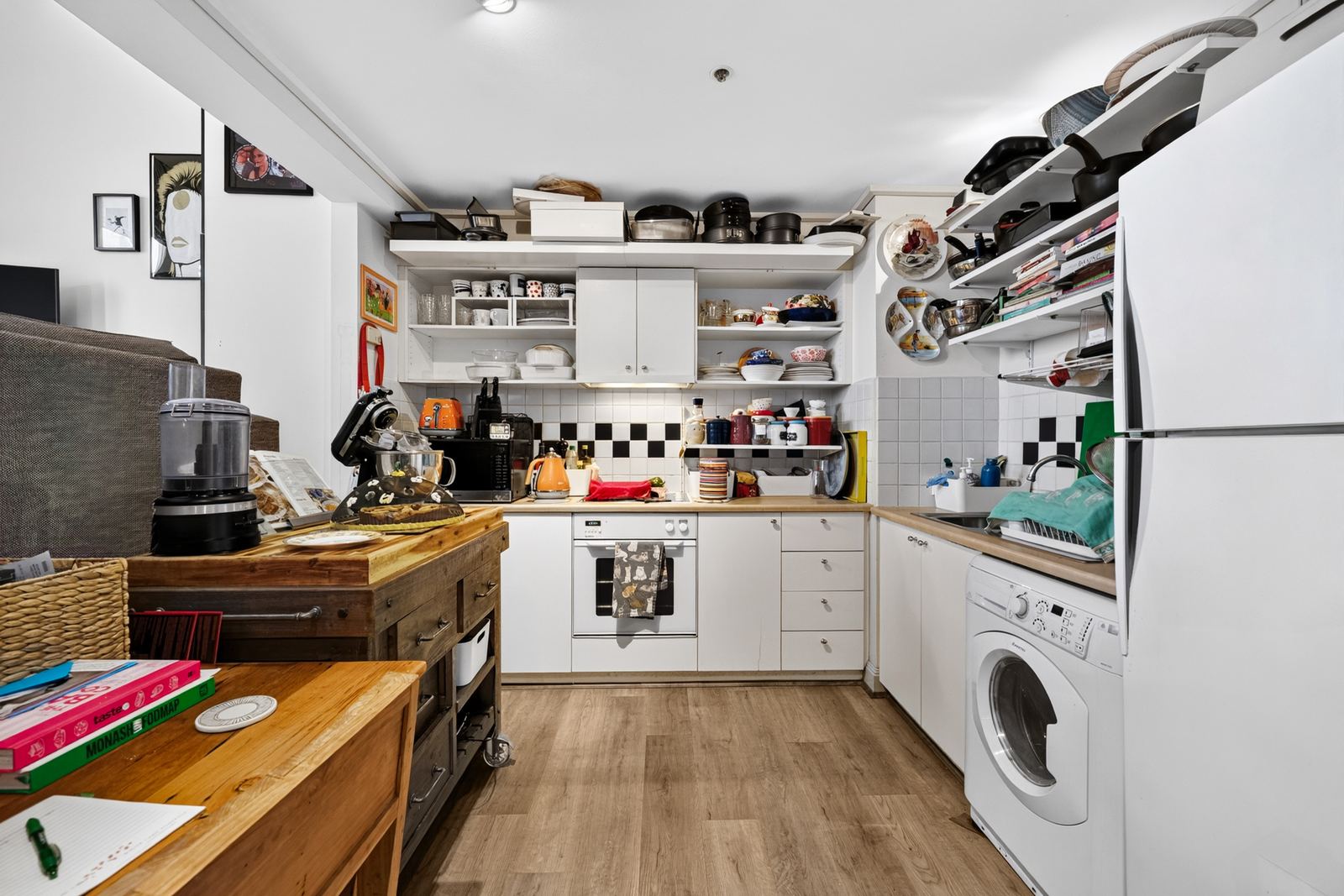 Virtual Staging Services 4 Occupied kitchen before virtual decluttering, with crowded open shelving and appliances across the benchtops
